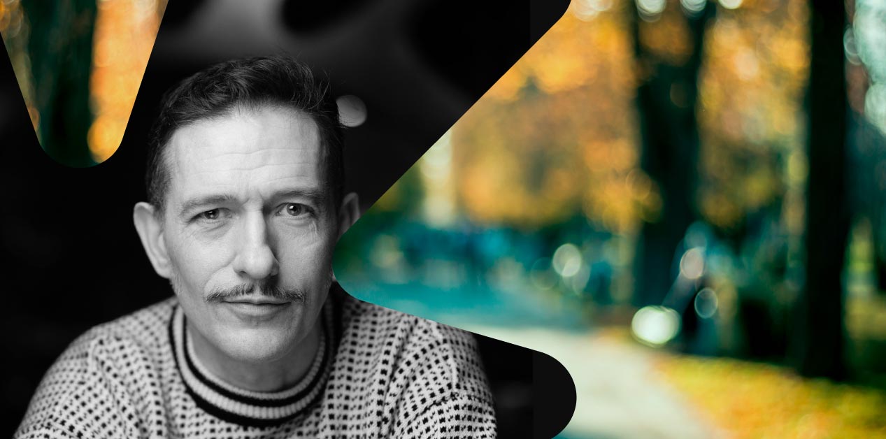 To bilder er koblet sammen. Et portrett av en person med kort hår og bart, iført mønstret genser. Det andre bildet en uskarp bakgrunn av høstløv og trær.